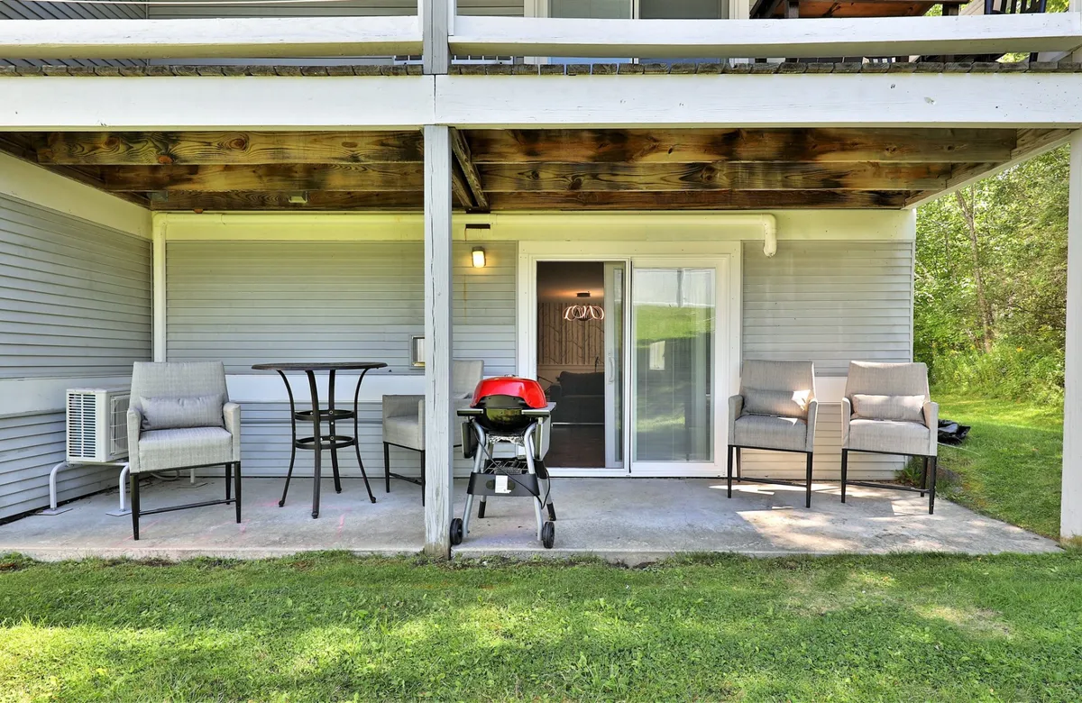 The image shows an outdoor seating area with comfortable chairs, a grill, and a sliding glass door, inviting guests to transition seamlessly between indoor comfort and outdoor relaxation.