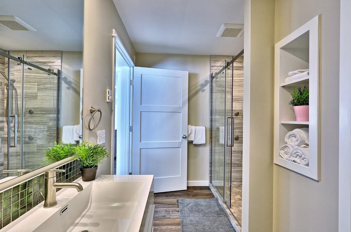 A modern bathroom featuring a glass shower enclosure, sleek sink, and subtle greenery on the countertop. Fresh towels are neatly arranged, and the overall space feels bright, refreshing, and spa-like—ideal for both relaxation and daily routines.