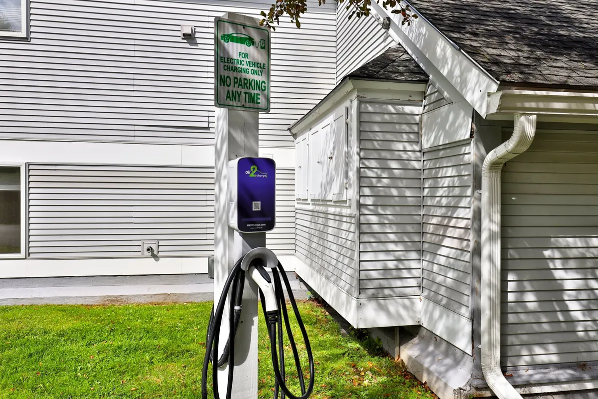 A modern exterior view featuring an electric vehicle charging station, clear signage, and the building facade. The scene suggests convenience and eco-friendliness within a well-maintained community setting.