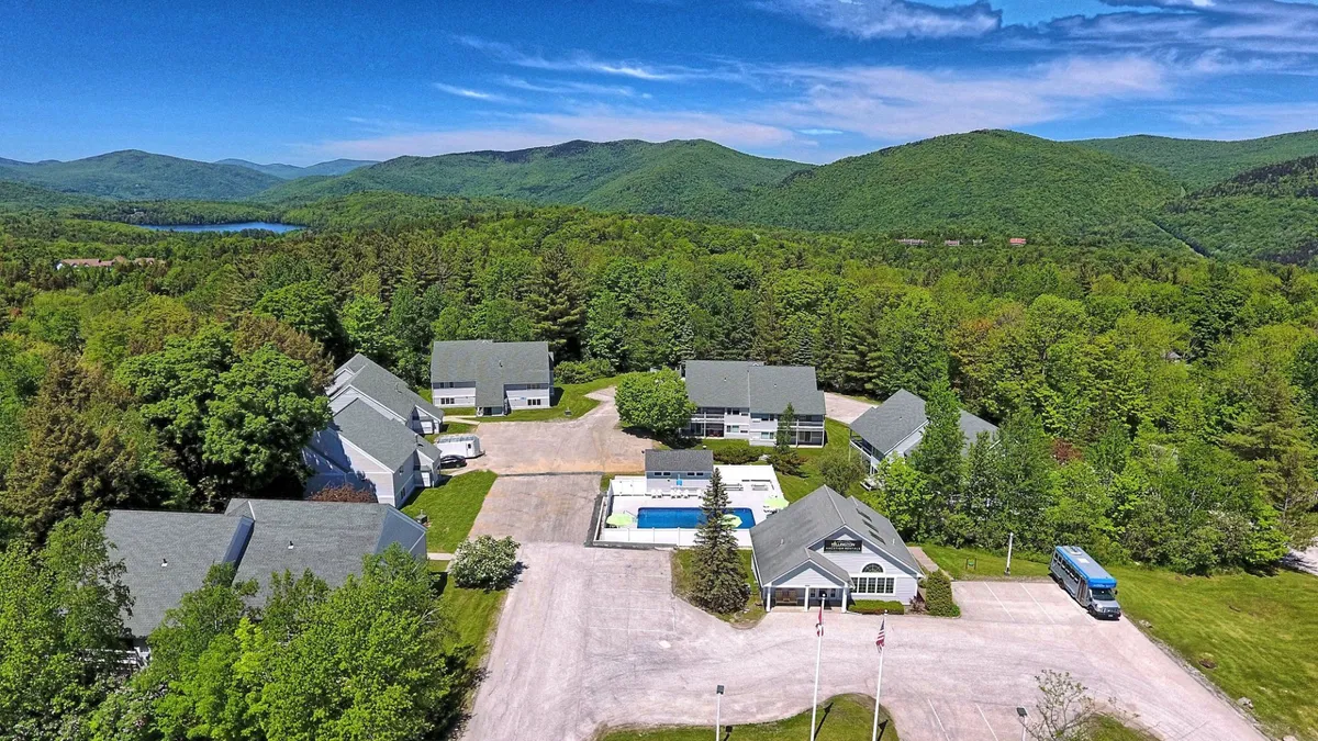 A serene outdoor scene featuring a large swimming pool, the main lodge, neatly arranged cabins, and the surrounding mountains. The tranquil atmosphere is ideal for summer gatherings, swimming, and enjoying stunning sunset views over the mountains.