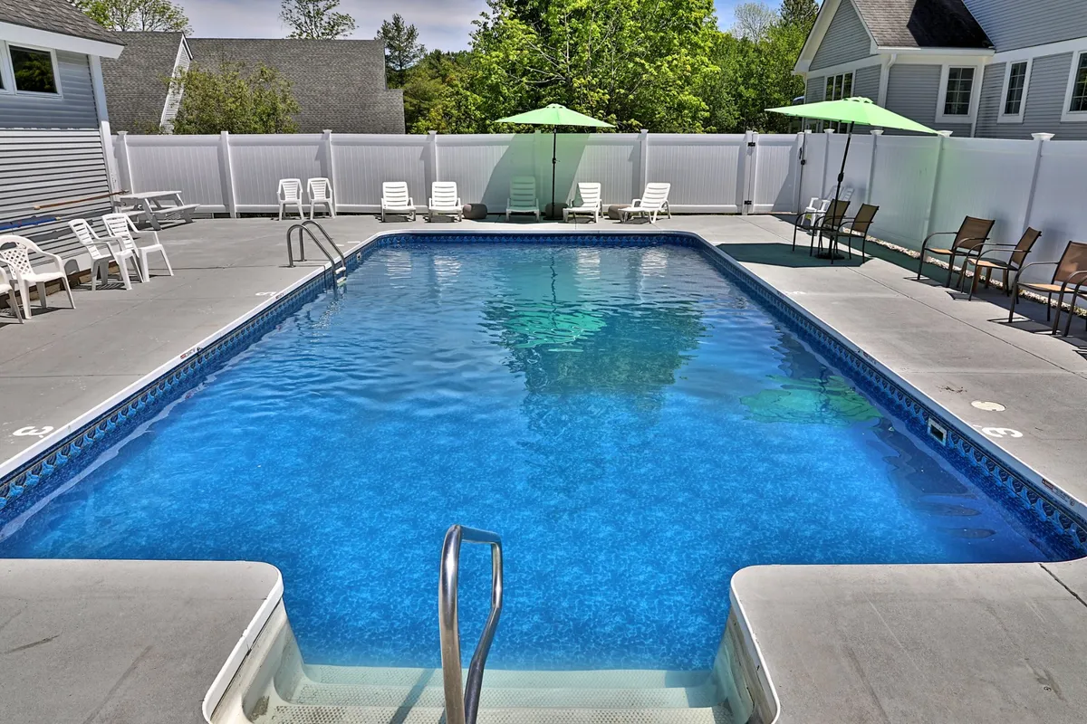 A sparkling swimming pool flanked by lounge chairs, umbrellas, and lush greenery, radiating a leisurely and refreshing ambiance. The setting is perfect for socializing or unwinding under the sun.