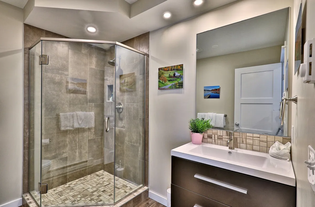 A bright, calming bathroom with a glass shower, contemporary vanity, and tasteful wall art. The space exudes tranquility and provides a comfortable area for grooming and relaxation, ideal for guests or family members needing a second full bathroom.