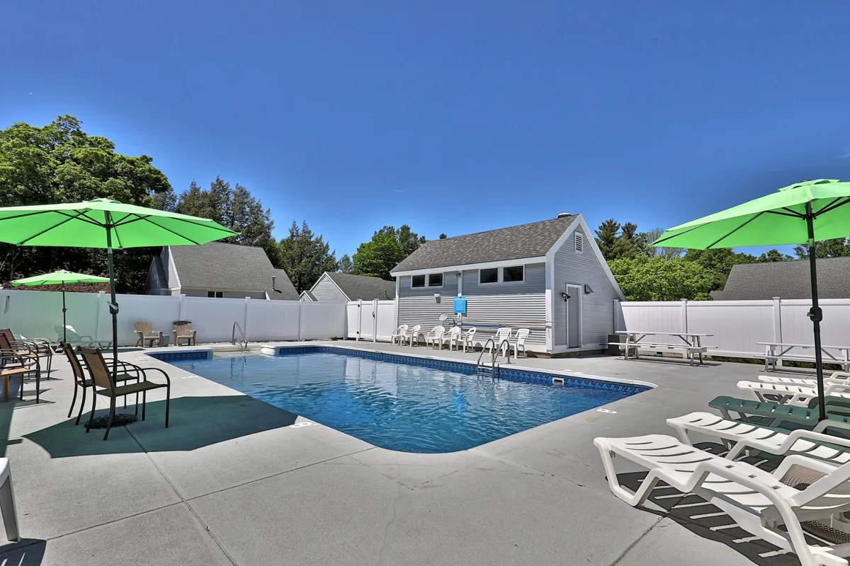 A vibrant outdoor swimming pool lined with green umbrellas and comfortable lounge chairs. The pool is adjacent to a poolside building and surrounded by lush greenery, creating a lively and inviting space for relaxation and fun under the sun.